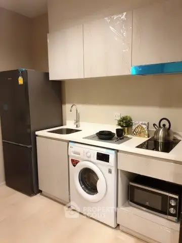Modern kitchen with sleek appliances including fridge, washing machine, and microwave in compact layout.