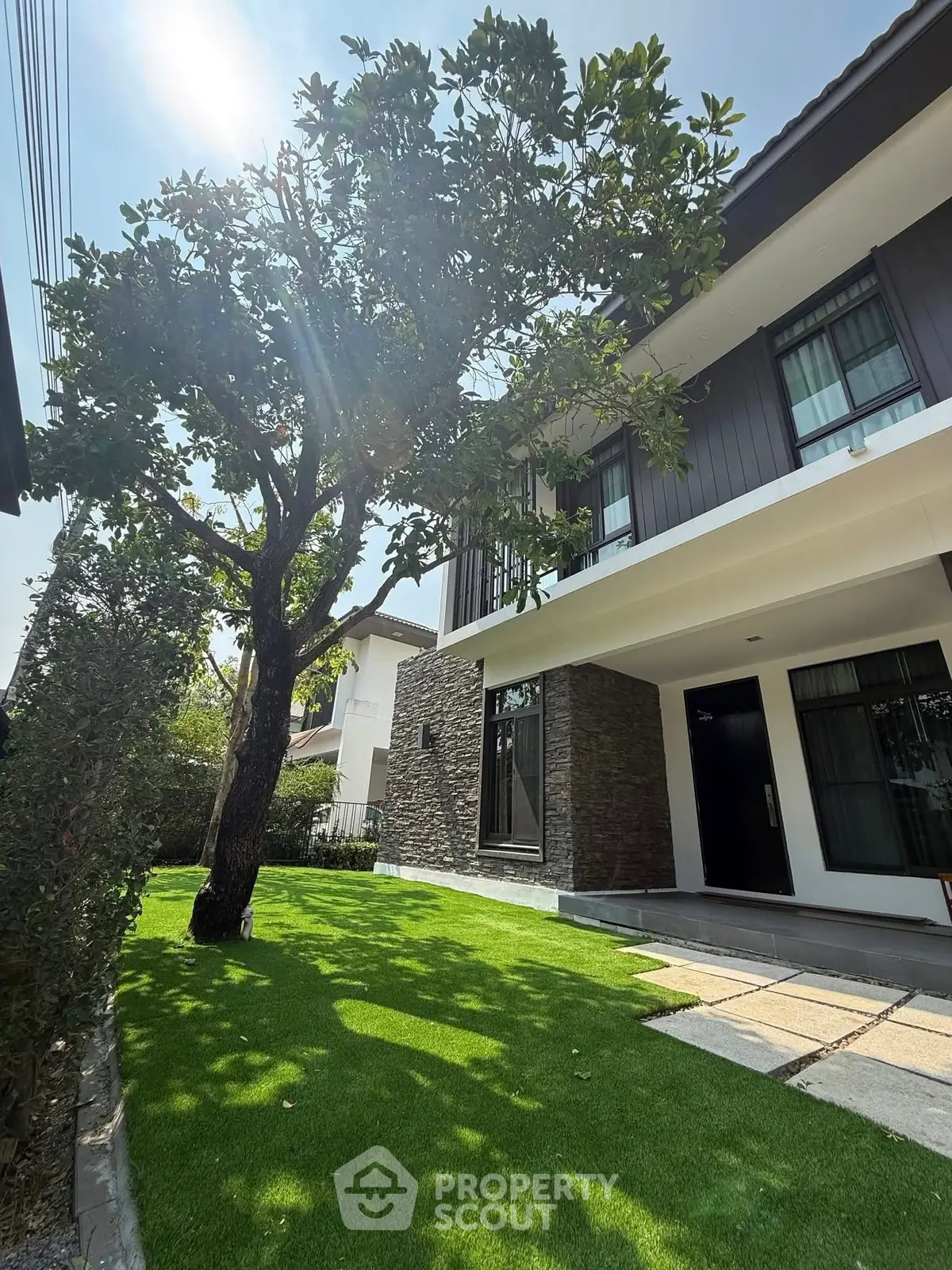 Modern two-story house with lush green lawn and mature tree, showcasing elegant exterior design.