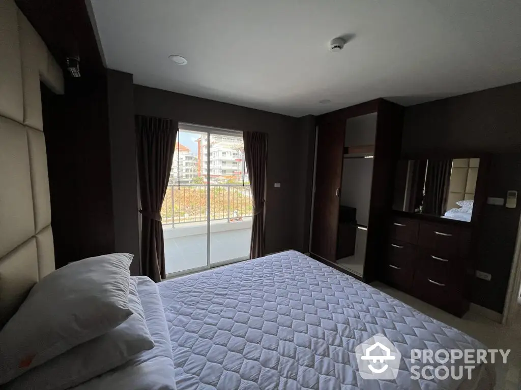 Spacious bedroom with large windows offering ample natural light and a view, complemented by dark elegant curtains and built-in storage.