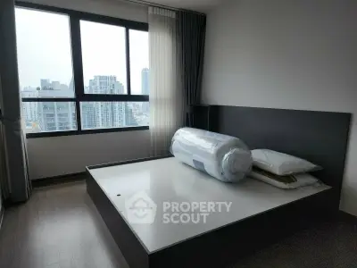 Modern bedroom with large window offering city view, featuring a sleek bed frame and minimalist decor.
