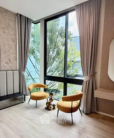 Modern living room with large window and stylish chairs, offering a serene view of greenery.