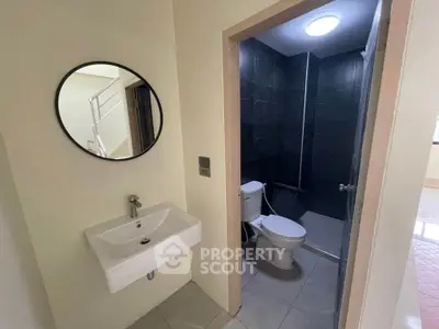 Modern bathroom with sleek sink and round mirror, adjacent to a compact toilet area.