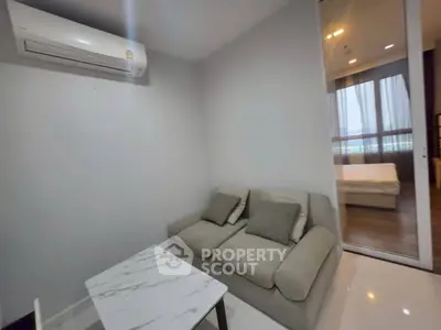 Modern living room with cozy sofa and air conditioning, adjacent to a bedroom with large windows.