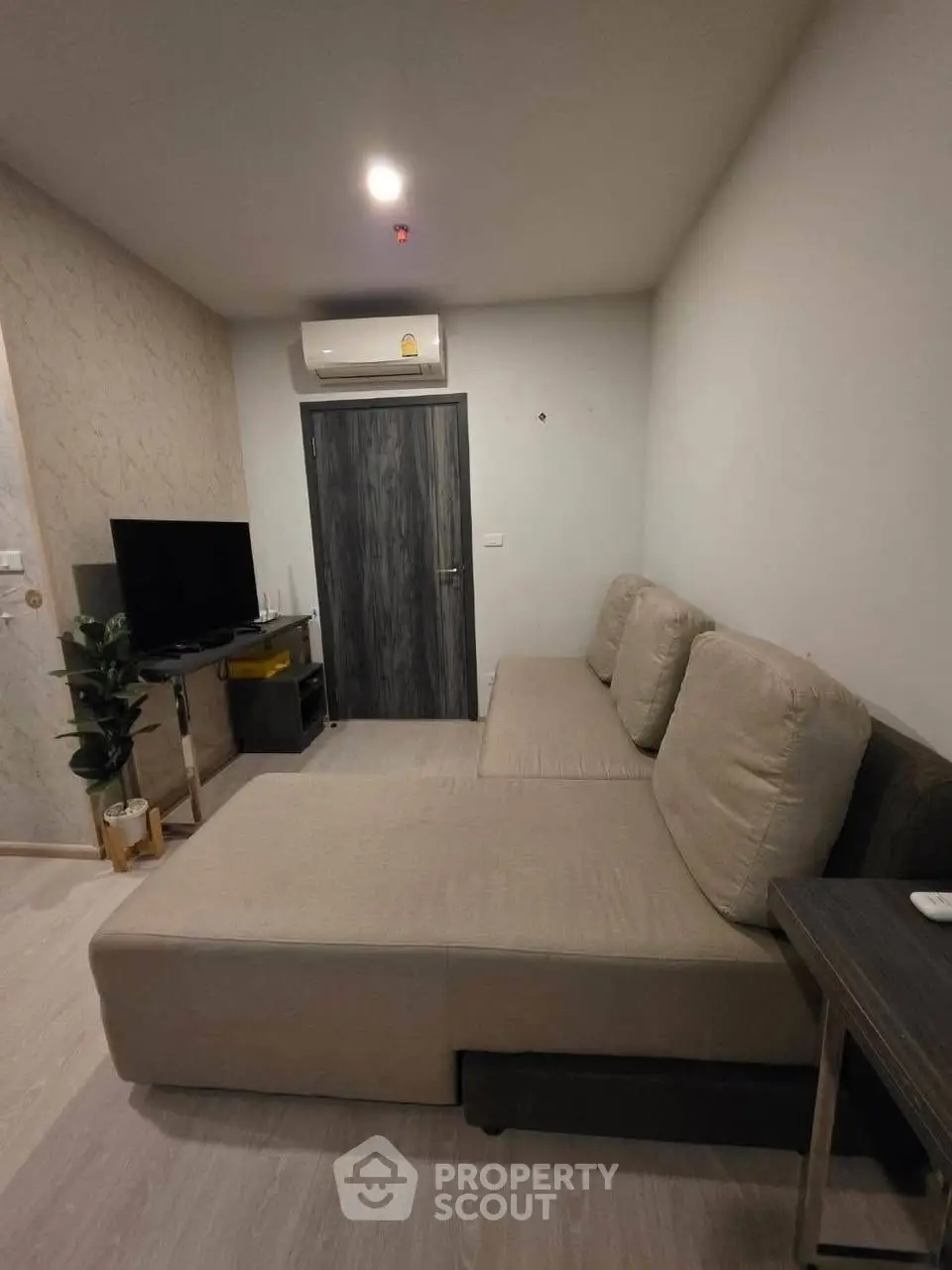 Modern living room with beige sofa and wall-mounted TV in cozy apartment.