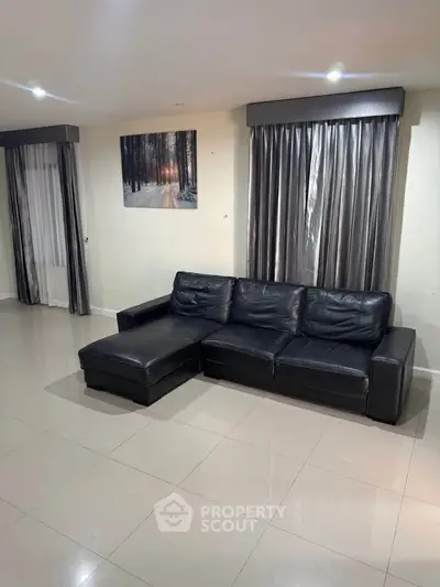 Spacious living room with sleek black leather sofa and elegant curtains, perfect for modern living.