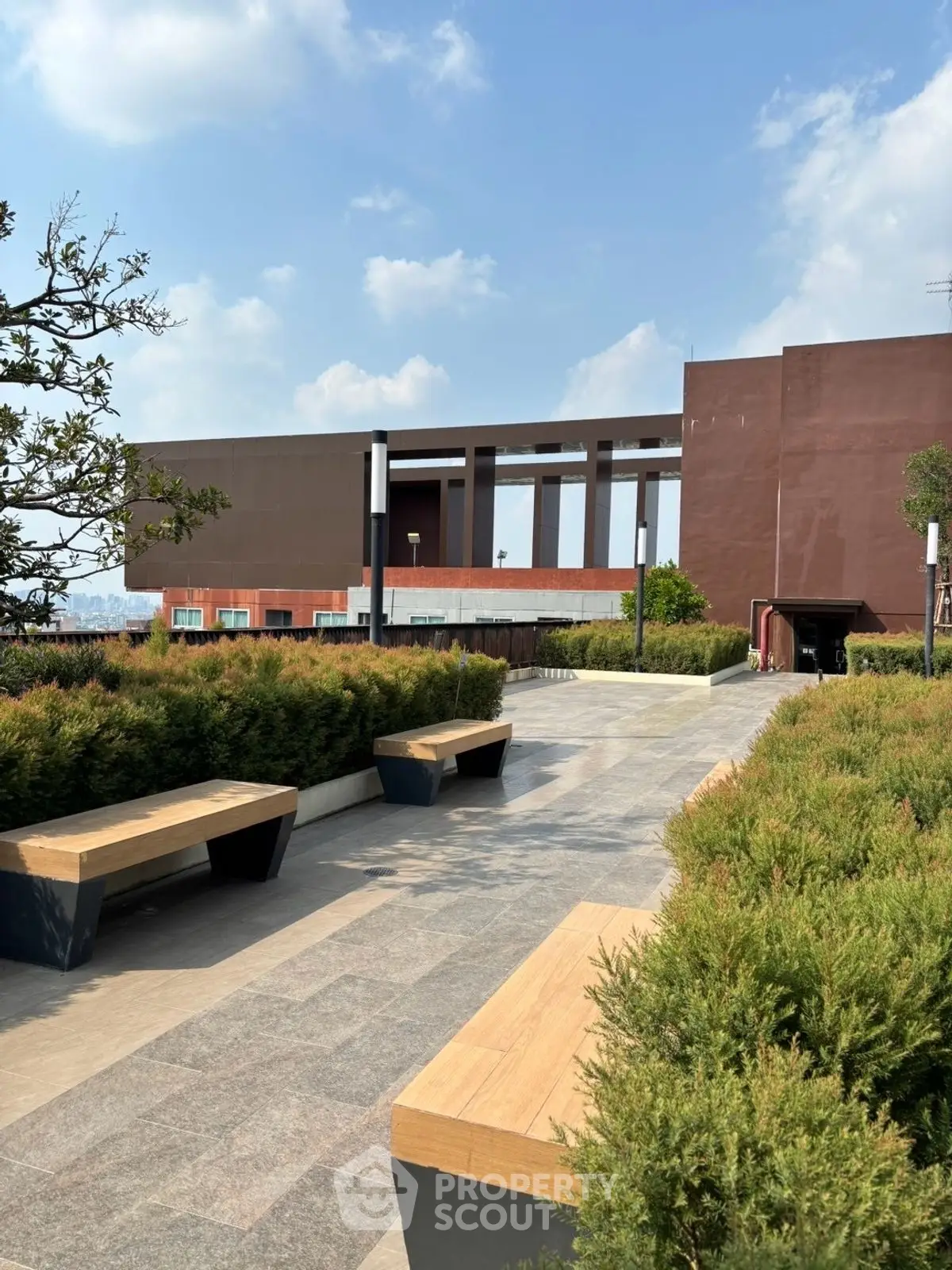 Modern rooftop garden with benches and lush greenery under a clear blue sky.