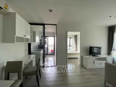 Modern apartment with open living area and kitchen, featuring sleek furniture and large windows.