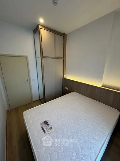 Modern bedroom with minimalist design and wooden flooring, featuring a cozy bed and built-in wardrobe.
