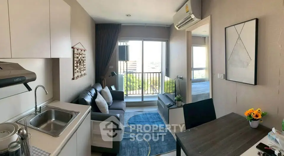 Modern apartment interior with open layout, featuring a cozy living room and kitchen area, leading to a balcony with city views.