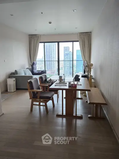 Spacious living room with city view, wooden furniture, and large windows for natural light.