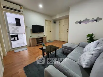 Modern living room with cozy gray sofa and sleek TV setup, adjacent to a compact kitchen.