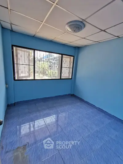 Spacious blue-walled room with large window and tiled floor, perfect for customization.