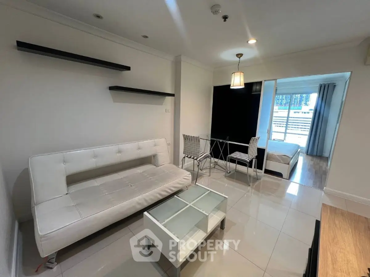 Modern living room with sleek white furniture and open view to bedroom