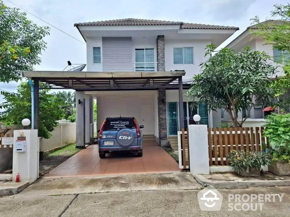 Charming two-story house with carport and lush greenery in a serene neighborhood.