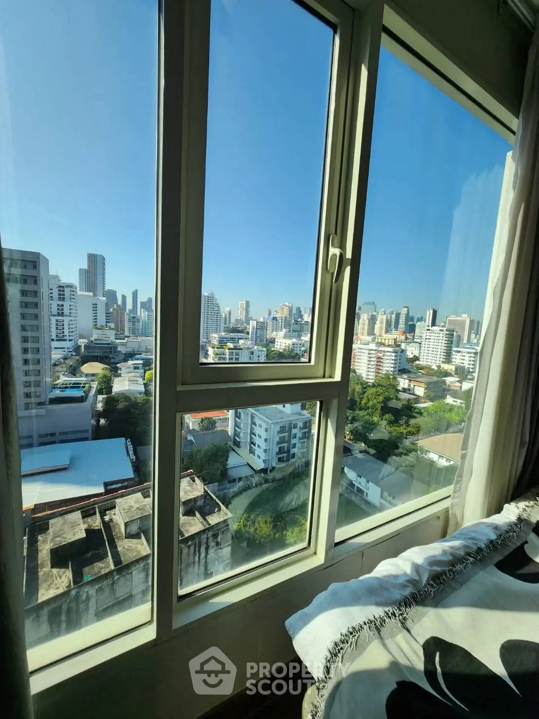 Stunning cityscape view from a high-rise apartment window, showcasing urban skyline and clear blue sky.