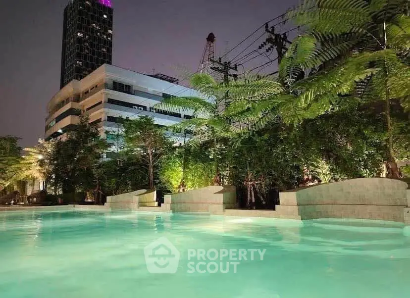 Luxurious night view of a modern building with a beautifully lit swimming pool and lush greenery.