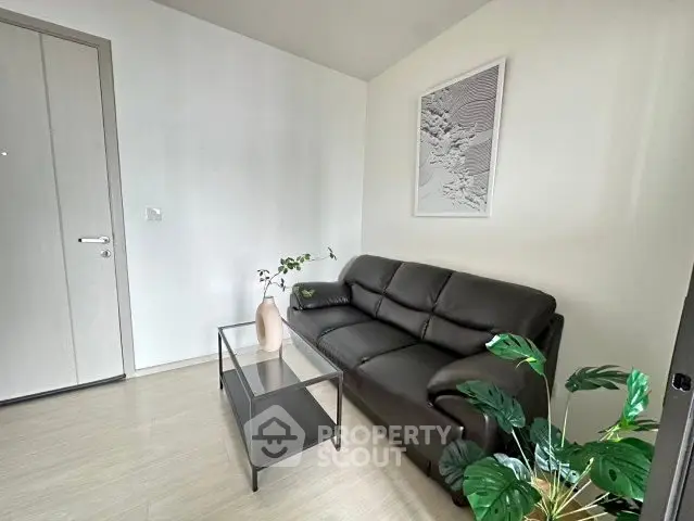 Modern living room with sleek black leather sofa and glass coffee table, minimalistic decor.