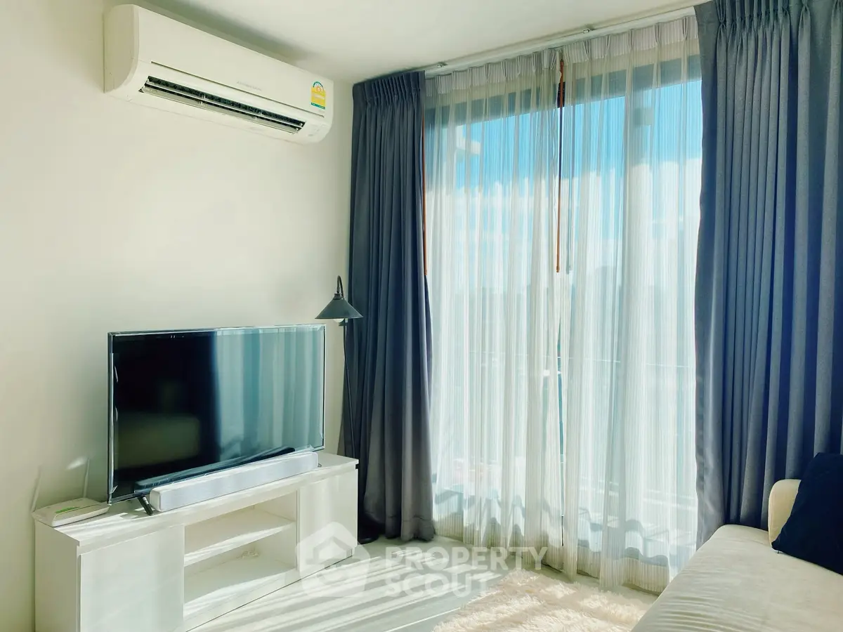Bright living room with large window, modern TV setup, and air conditioning unit.