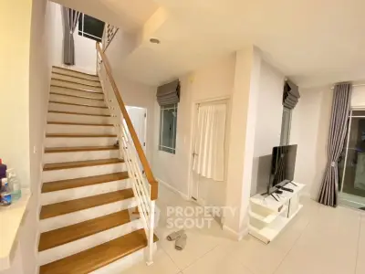 Modern living room with staircase and TV, featuring sleek design and bright lighting.