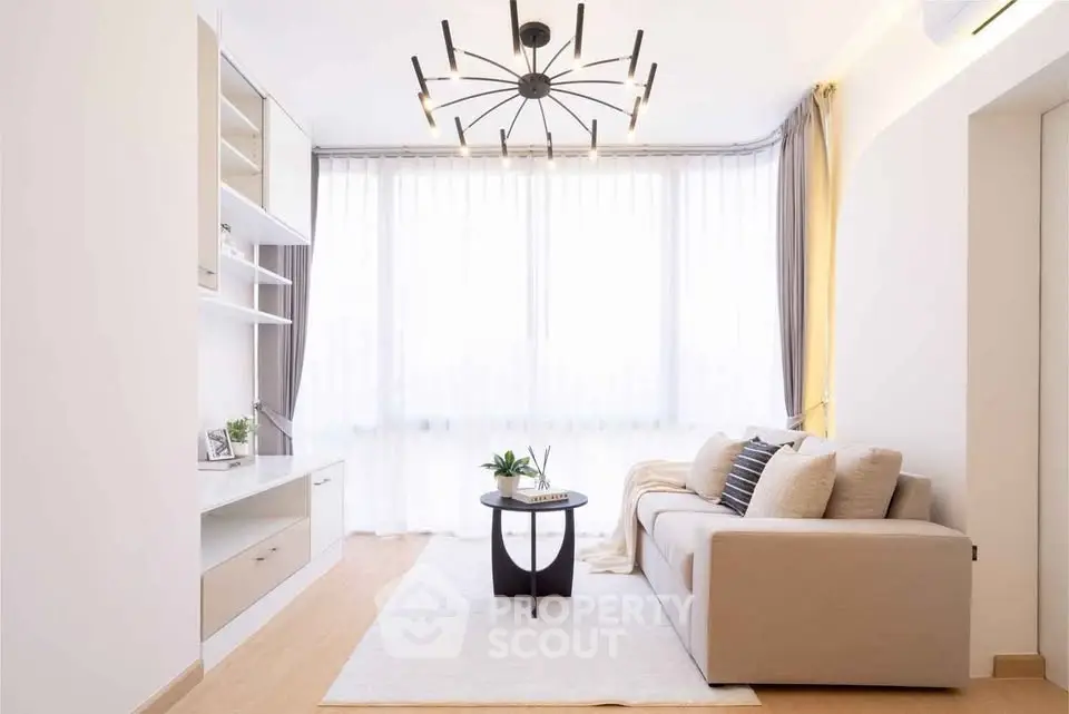 Modern living room with elegant chandelier and cozy sofa, featuring floor-to-ceiling windows and stylish decor.