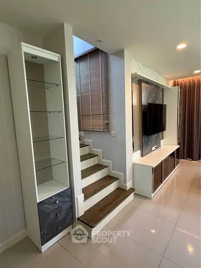 Modern living room with sleek staircase and built-in TV unit, showcasing contemporary design and functionality.