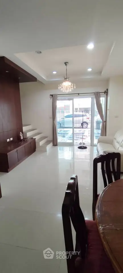 Spacious living room with elegant chandelier and large windows offering natural light.