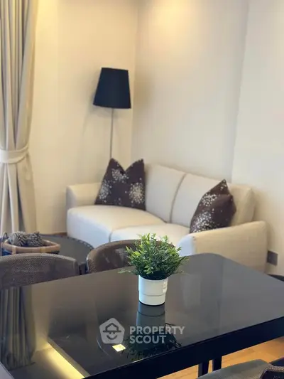 Cozy living room with modern decor, featuring a stylish sofa, elegant lamp, and a chic glass table.