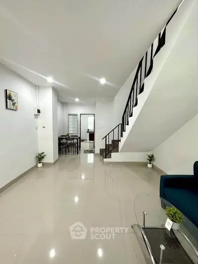Modern living room with staircase and dining area, featuring sleek design and bright lighting.