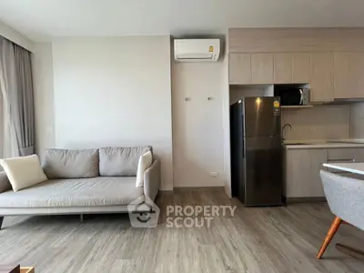Modern living room with sleek kitchen and stylish sofa, featuring wood flooring and neutral tones.