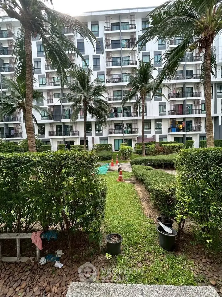 Modern apartment building with lush garden and palm trees, offering serene outdoor living space.