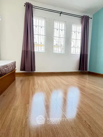 Spacious bedroom with polished wooden floors and large windows for natural light.