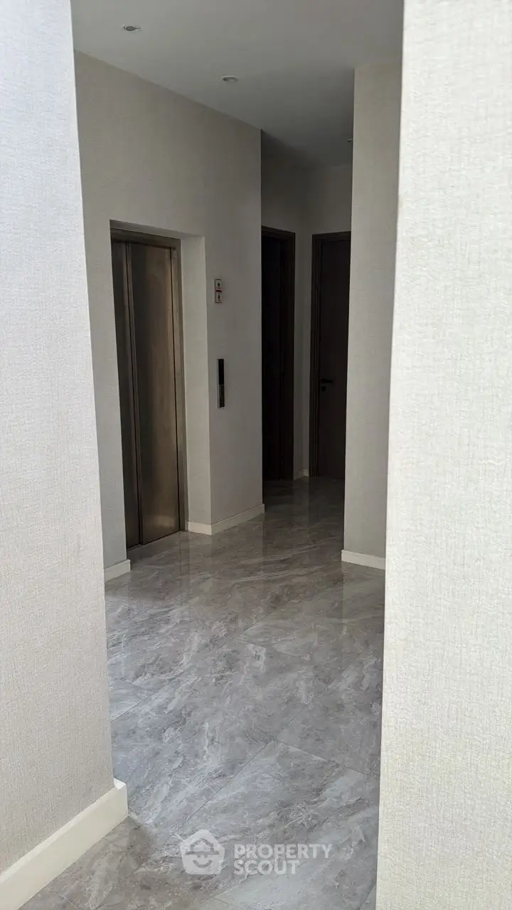 Modern building corridor with sleek elevator and polished marble flooring.