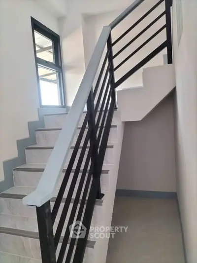 Modern staircase with sleek black railing and marble steps in a bright interior space.