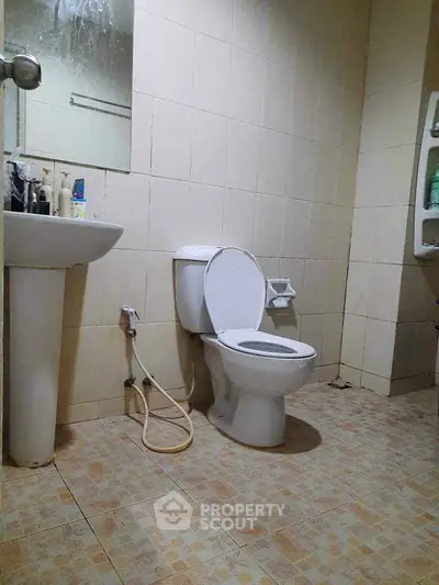 Simple bathroom with tiled walls and floor, featuring a toilet and sink.