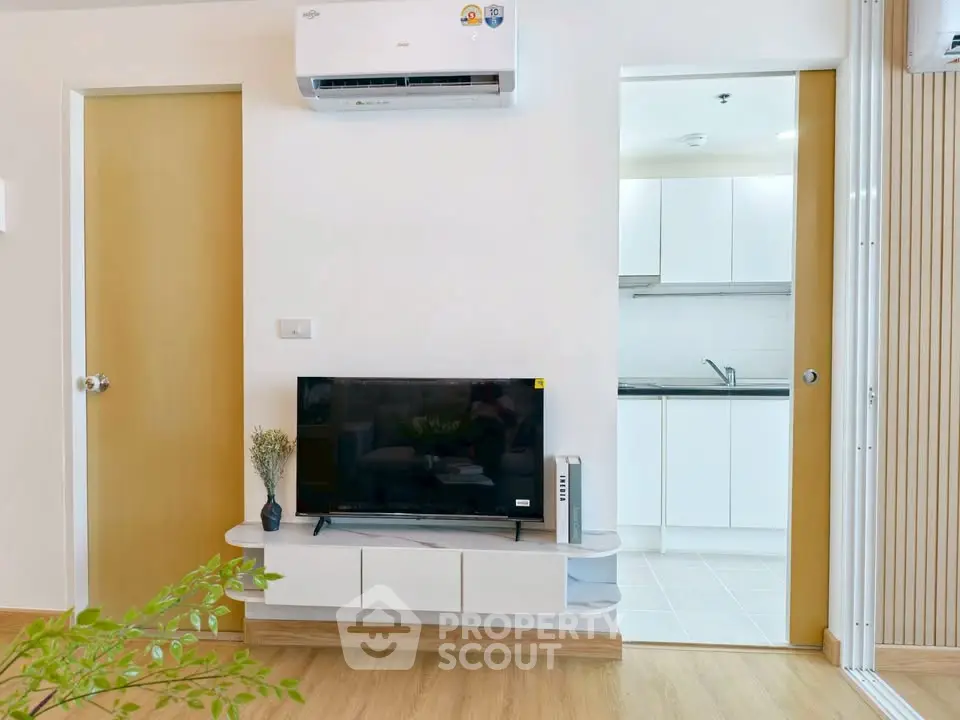 Modern living room with TV and air conditioning, open view to sleek kitchen.