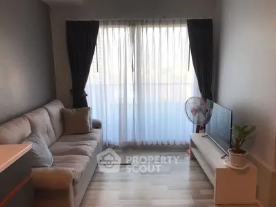Cozy living room with modern sofa and TV, featuring large window with curtains.