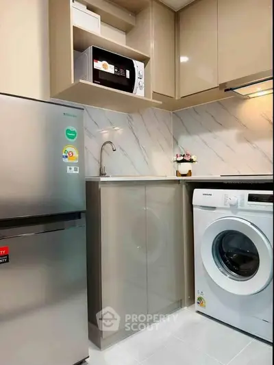Modern kitchen with sleek appliances including fridge, microwave, and washing machine in compact layout.