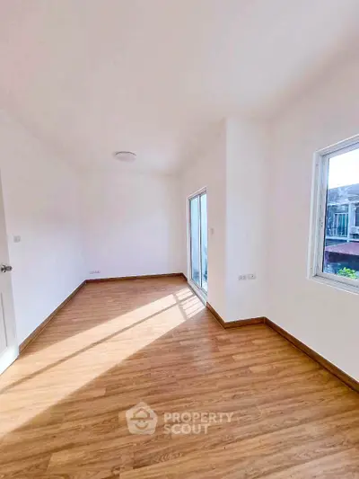 Spacious sunlit room with wooden flooring and large windows in modern home.