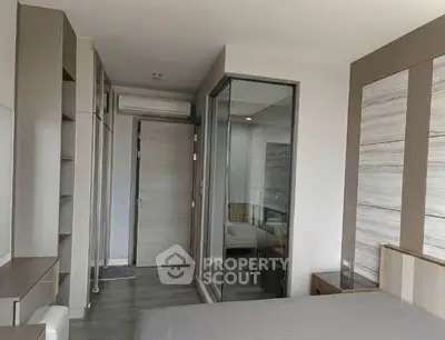 Modern bedroom with sleek design and glass partition, featuring neutral tones and stylish furnishings.