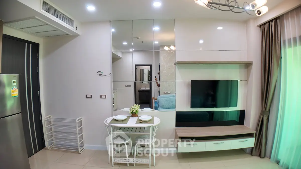 Modern living room with mirrored wall, dining table, and TV setup in a cozy apartment.