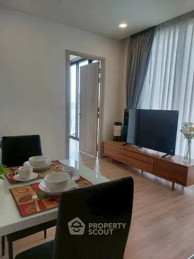 Modern living room with dining area and large TV, featuring elegant decor and natural light.