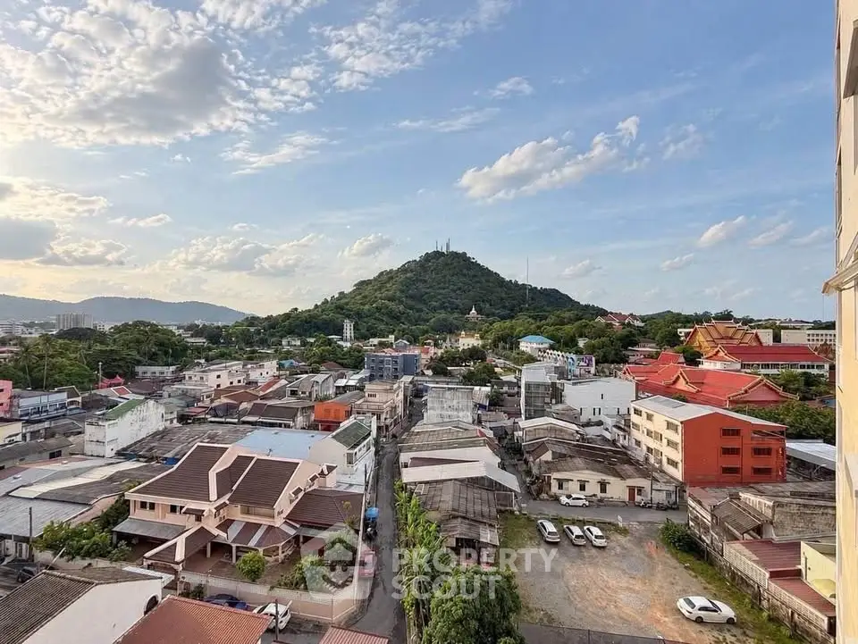Scenic cityscape view with lush green hill and residential buildings under a clear blue sky.