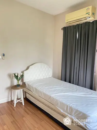 Cozy bedroom with polished wooden flooring, elegant white bed, and modern air conditioning unit, complemented by stylish gray curtains.