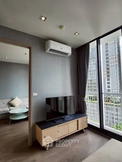 Modern living room with large windows and city view, featuring sleek furniture and air conditioning.