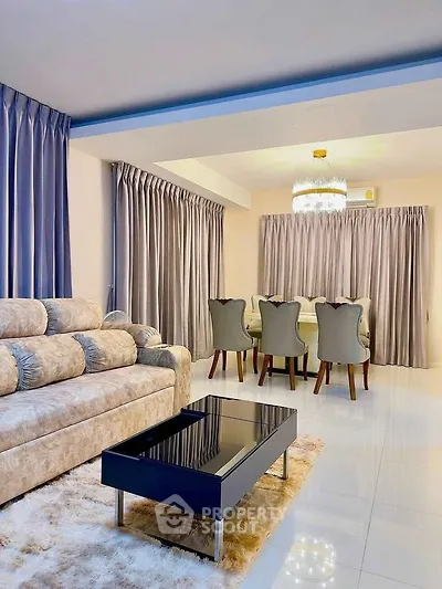 Luxurious living room with plush sofa and elegant dining area, featuring modern chandelier and sleek decor.
