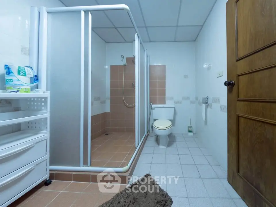 Spacious bathroom with shower and toilet, featuring tiled flooring and wooden door.