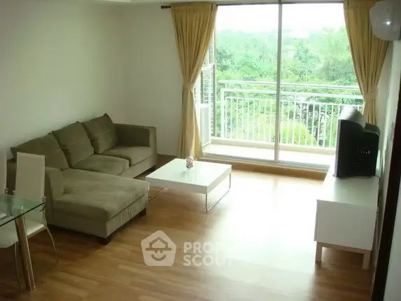 Spacious living room with large window and balcony view, featuring modern furniture and wooden flooring.