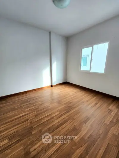 Spacious empty room with wooden flooring and natural light from window