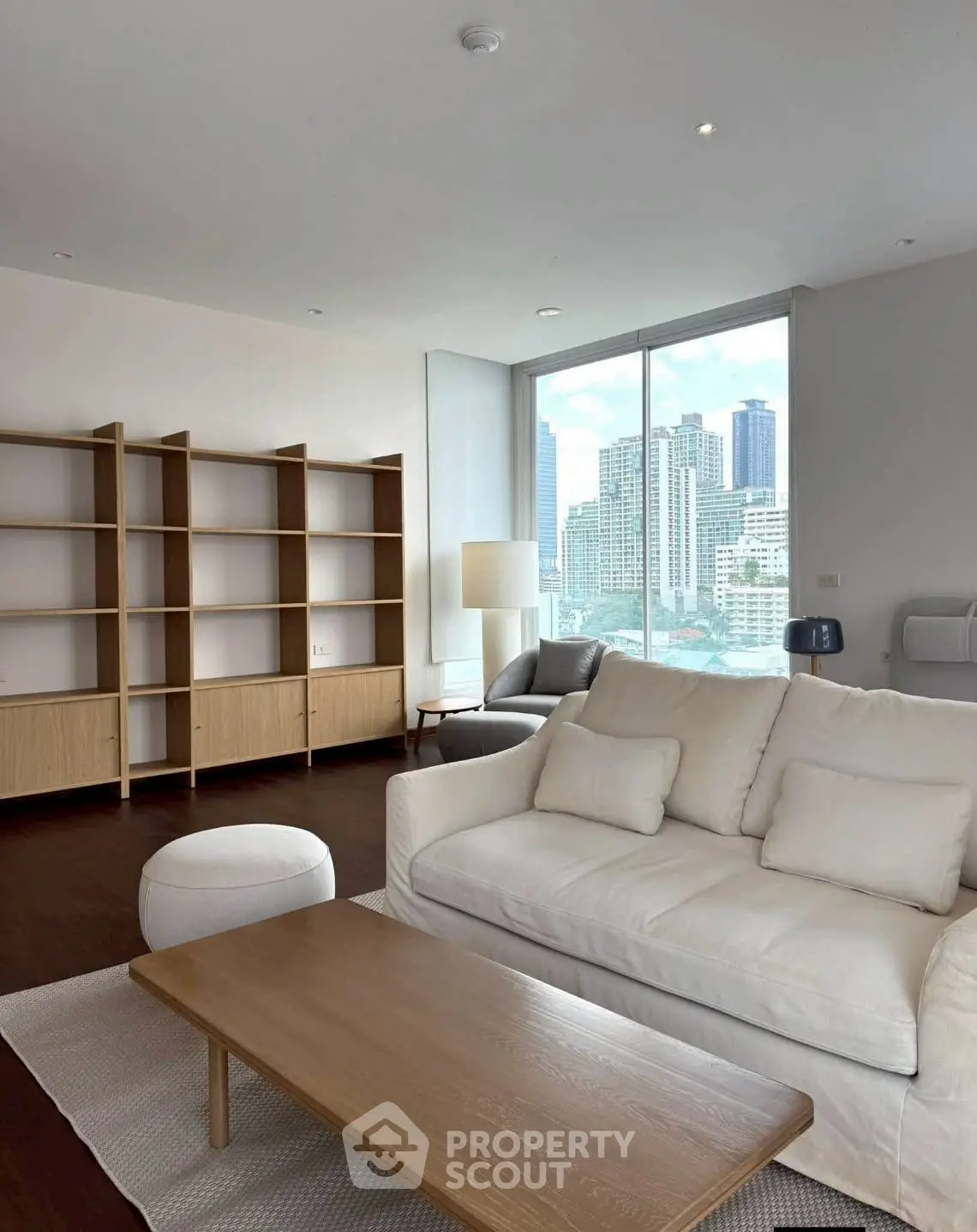Spacious living room with modern furniture and city view, featuring a cozy white sofa and wooden shelves.