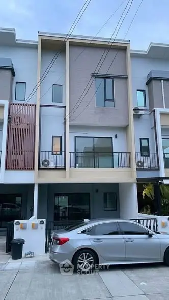 Modern three-story townhouse with sleek design and balcony, featuring a parked car in the driveway.
